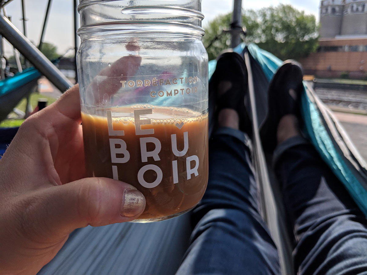 drinking coffee from a mason jar in a hammock. Le Bruloir printed on jar
