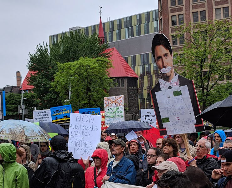 Anti pipeline protest in the rain, large justin trudeau sign and other stop kinder morgan signs